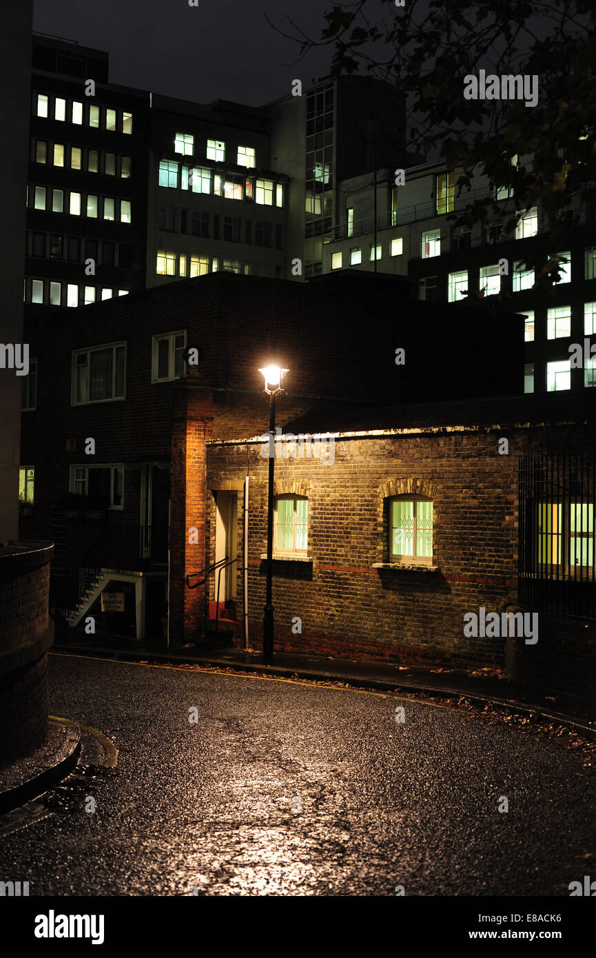 Un vecchio acciottolato bagnate Street a Londra illuminata da un lampione con moderni edifici per uffici in background Foto Stock