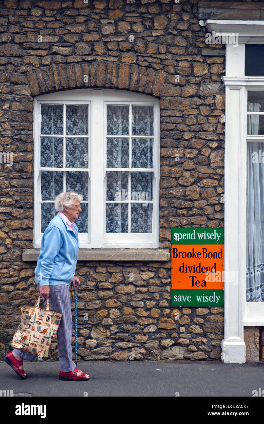 Un pensionato residente passeggiate passato un vecchio segno di stagno nel Somerset villaggio di Bruton REGNO UNITO Foto Stock