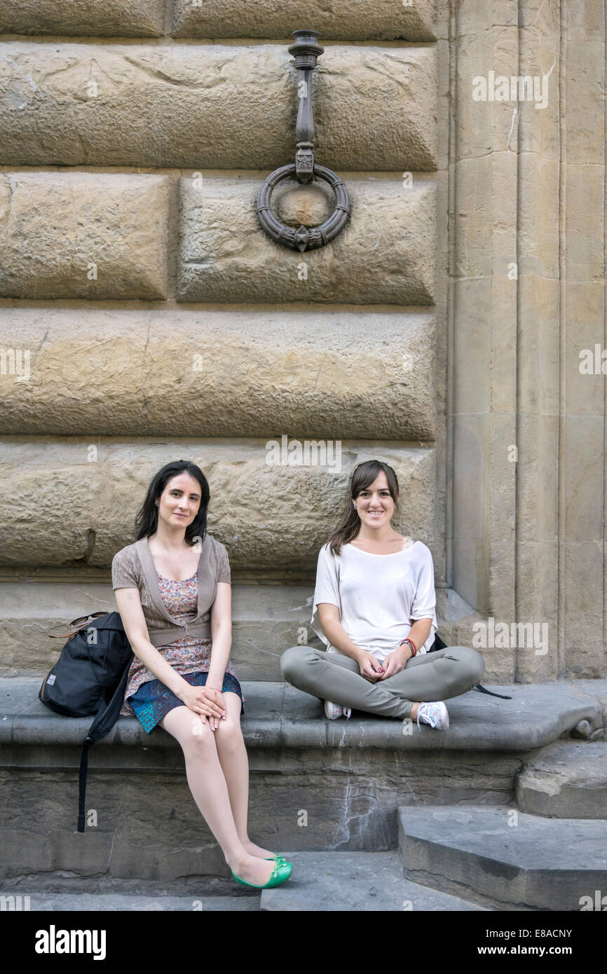 Due giovani abbastanza visitatori europei a Firenze demurely relax nella Piazza di San Firenze alla base di un vecchio edificio Foto Stock