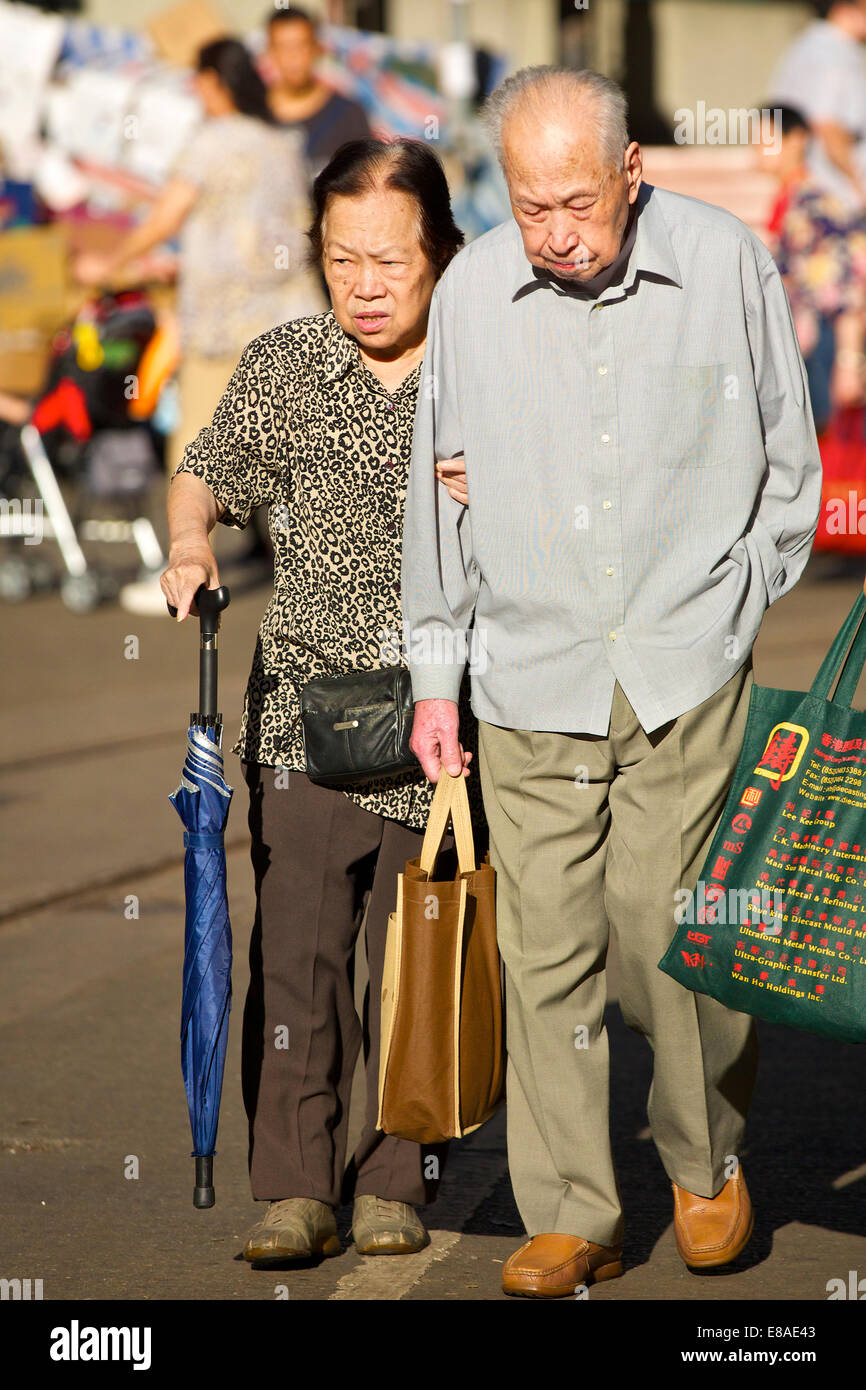 Vecchia coppia cinese si aiutano a vicenda di attraversare la strada su Chun Yeung Street, North Point, Hong Kong. Foto Stock