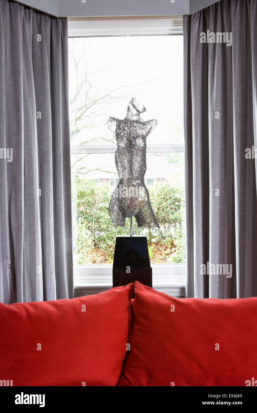 Mesh scultura figurativa di fronte soggiorno finestra con grigio metallico tende e divano rosso Foto Stock