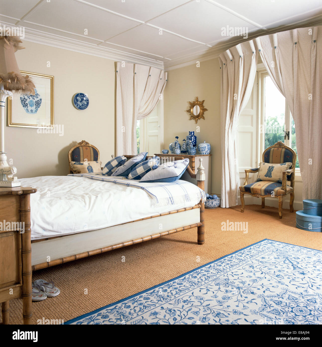 La crema pinch-pieghettato tende alle finestre in camera da letto con cuscini controllati sulla cornice di bamboo bed Foto Stock