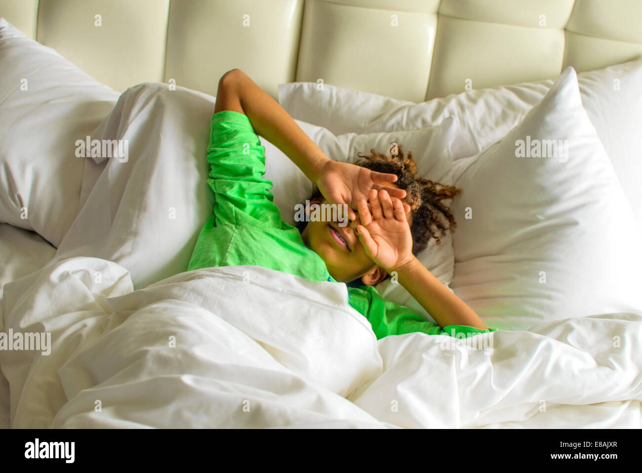 Sleepy boy giacente in letto faccia di schermatura con le mani Foto Stock
