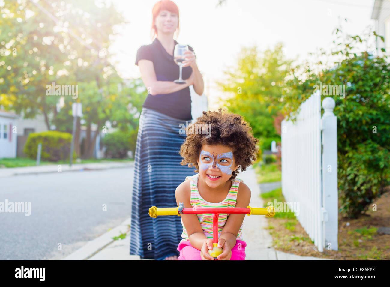 Ragazza con faccia dipinta accovacciato su scooter su strada suburbana Foto Stock