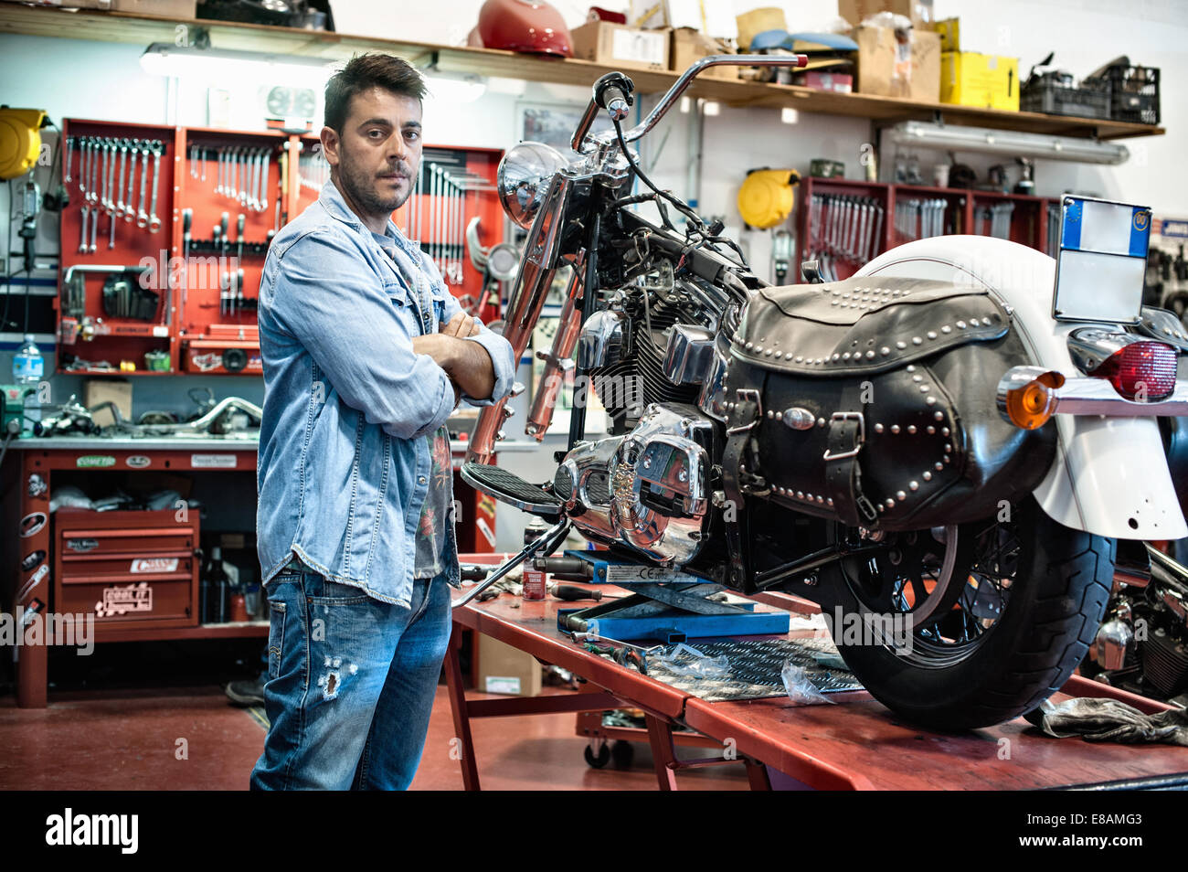 Ritratto di meccanico maschio con le braccia incrociate in motocicletta workshop Foto Stock