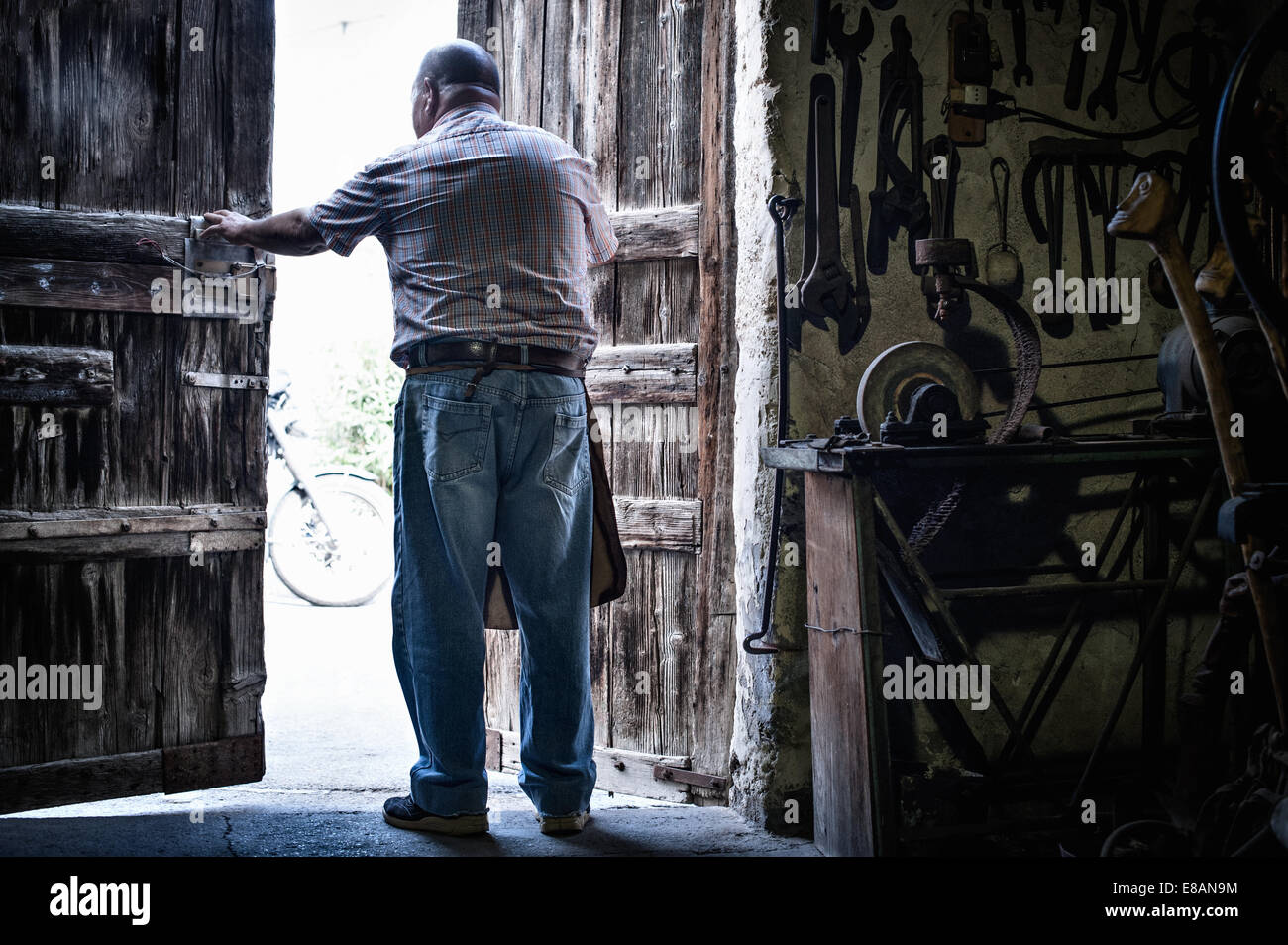 Vista posteriore del maschio anziano fabbro in apertura di sportelli della tradizionale granaio, Cagliari, Sardegna, Italia Foto Stock