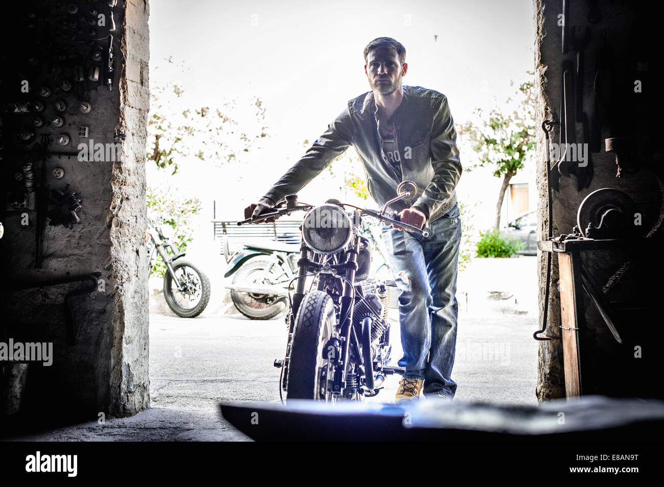 Metà uomo adulto spingendo motocicletta attraverso il fienile porta Foto Stock