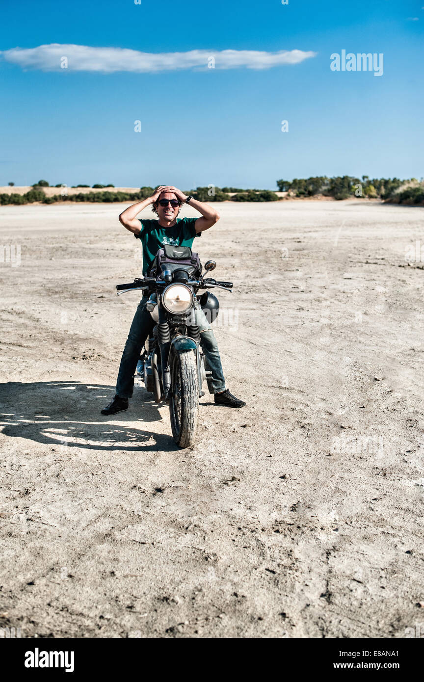 Metà uomo adulto seduto sul motociclo su arida pianura, Cagliari, Sardegna, Italia Foto Stock
