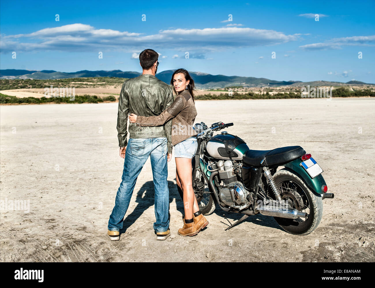 Vista posteriore della coppia giovane e motociclo su arida pianura, Cagliari, Sardegna, Italia Foto Stock