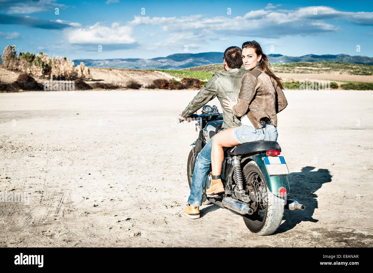 Vista posteriore della coppia giovane riding motociclo su arida pianura, Cagliari, Sardegna, Italia Foto Stock