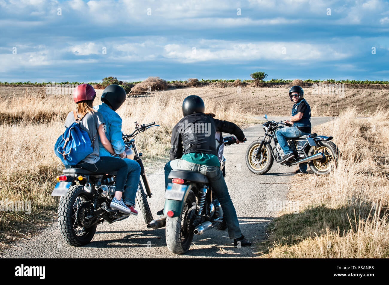 Vista posteriore di quattro amici chattare su motocicli sulla strada rurale, Cagliari, Sardegna, Italia Foto Stock