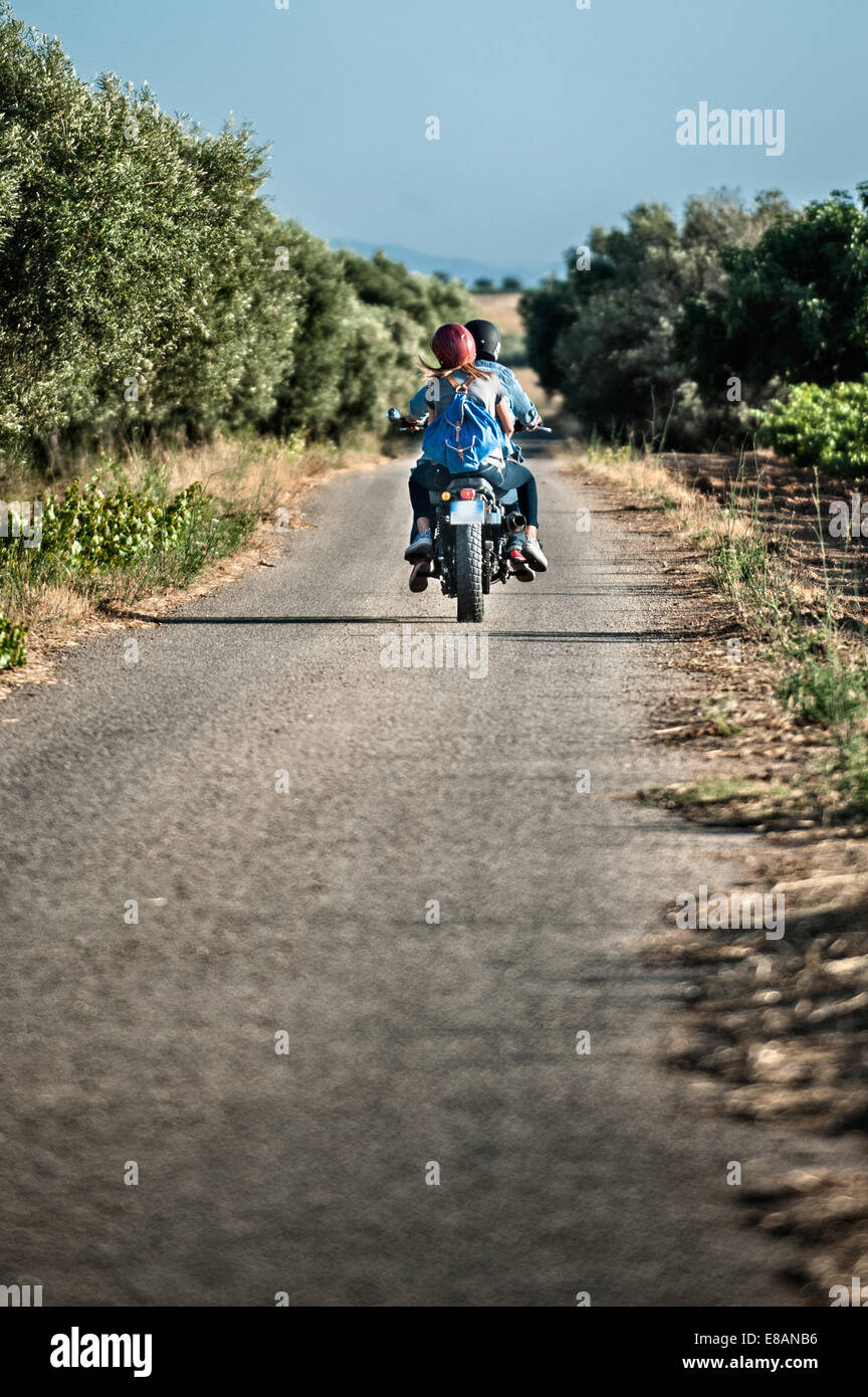 Vista posteriore della metà adulto giovane in sella motocicletta sulla strada rurale, Cagliari, Sardegna, Italia Foto Stock