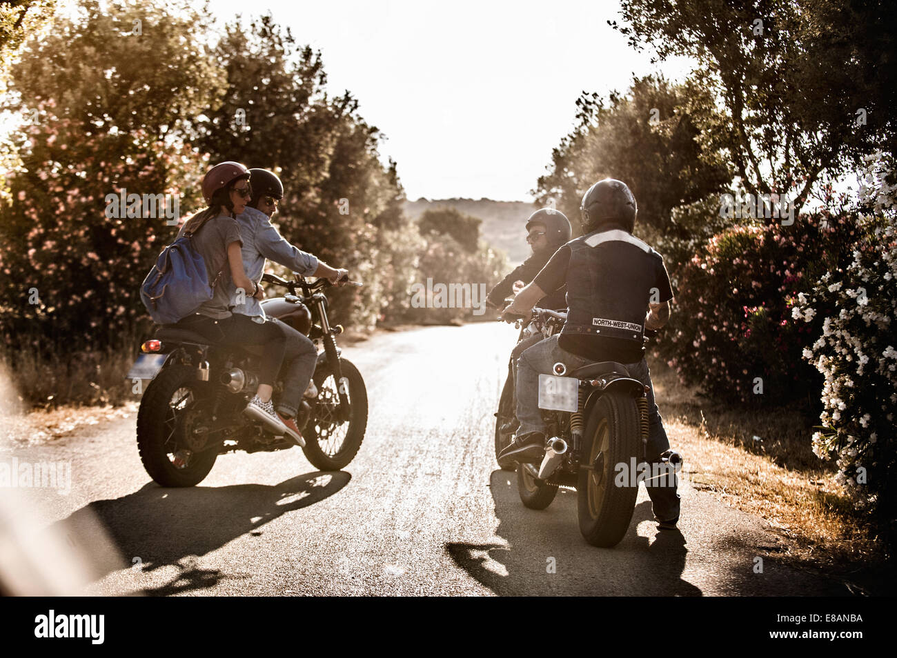 Vista posteriore di quattro amici su motocicli chattare su strada rurale, Cagliari, Sardegna, Italia Foto Stock