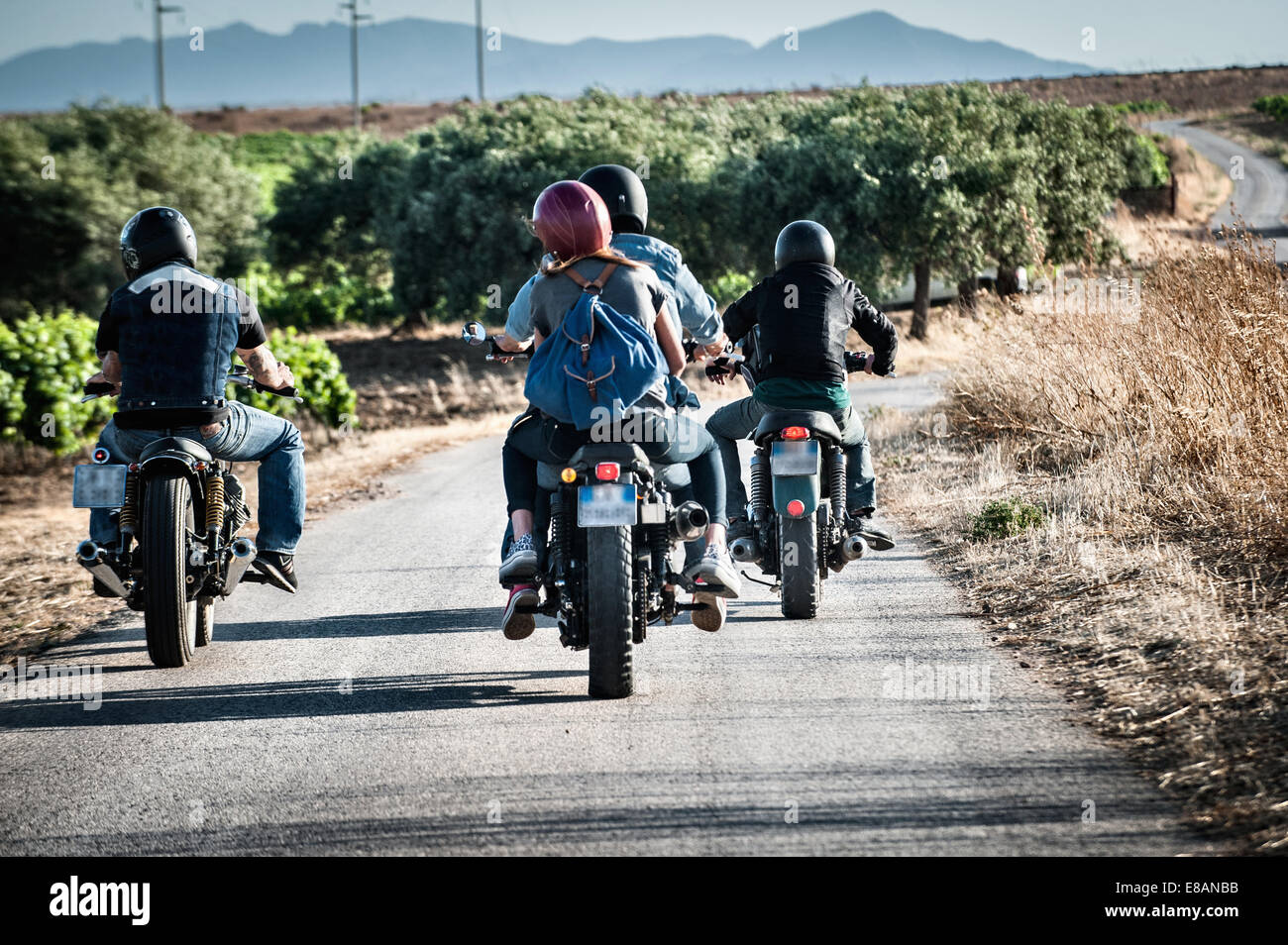 Vista posteriore di quattro amici motociclismo su strada rurale, Cagliari, Sardegna, Italia Foto Stock