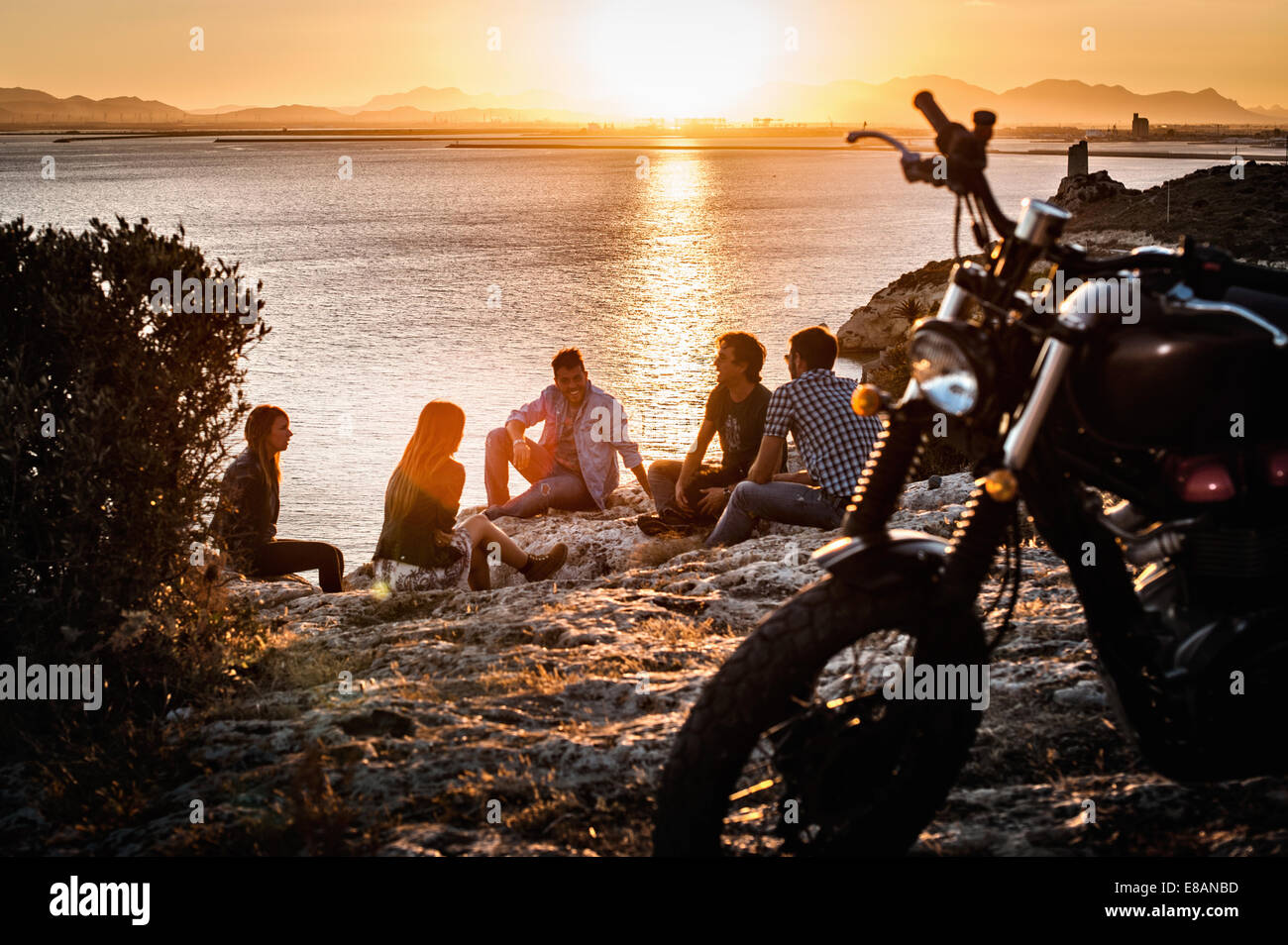 Cinque amici di motociclismo prendendo una pausa sulla costa al tramonto, Cagliari, Sardegna, Italia Foto Stock