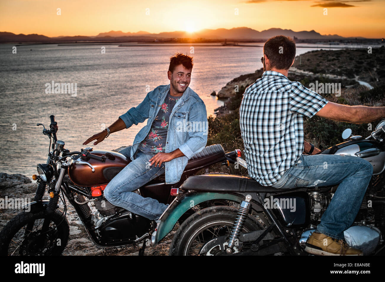 Ritratto di due maschi amici motociclisti sulla costa al tramonto, Cagliari, Sardegna, Italia Foto Stock