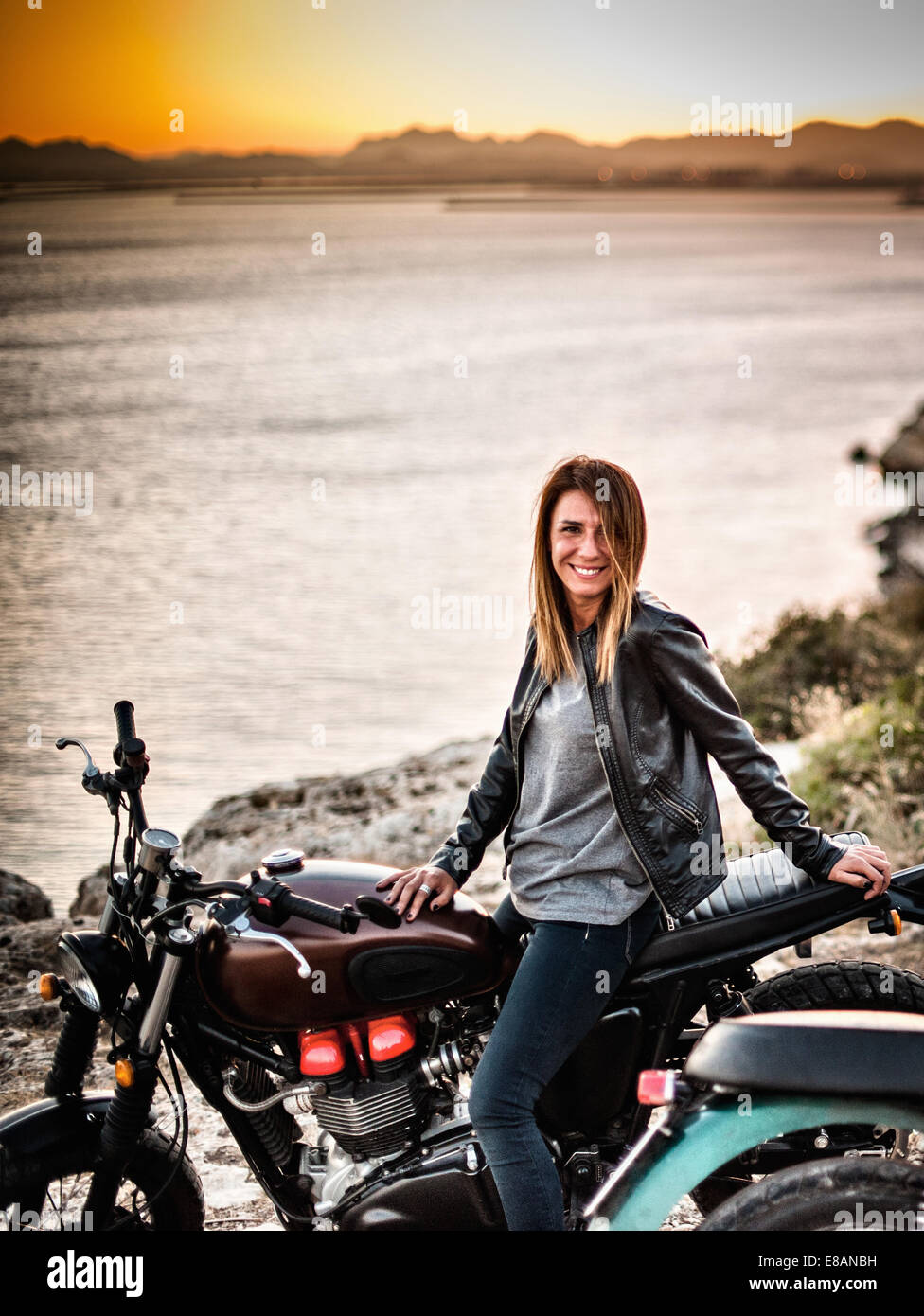 Ritratto di metà femmina adulta del motociclista sulla costa al tramonto, Cagliari, Sardegna, Italia Foto Stock