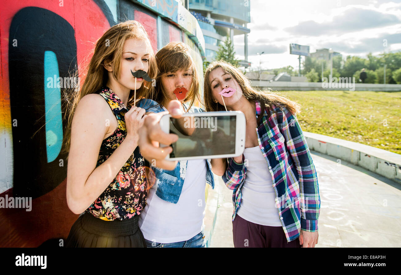 Amici prendendo selfie indossano false labbra e baffi, murale in background Foto Stock Amici prendendo selfie indossano false labbra e baffi, murale in background Foto Stock