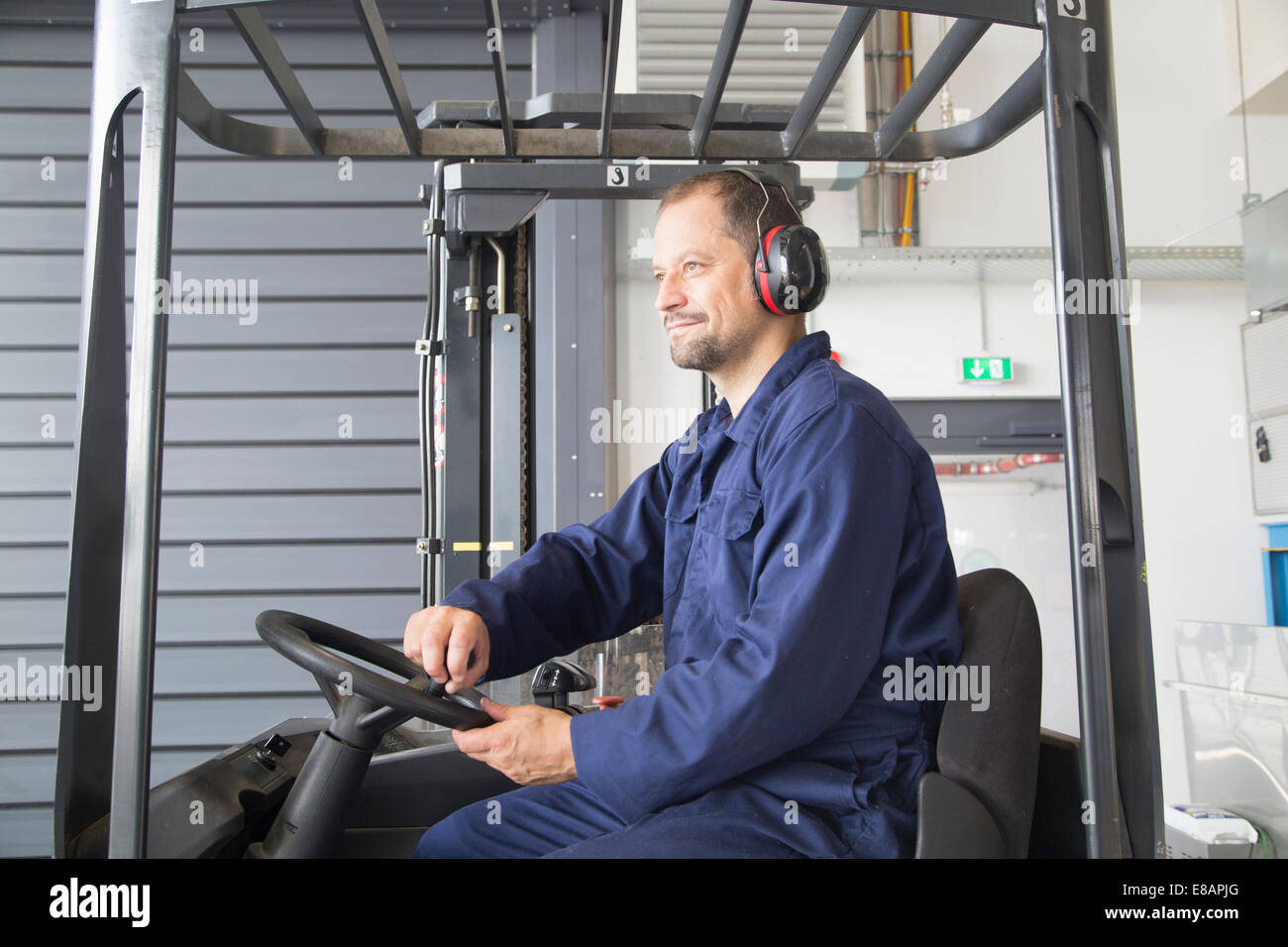 Lavoratore nel carrello elevatore a forche in impianto industriale Foto Stock