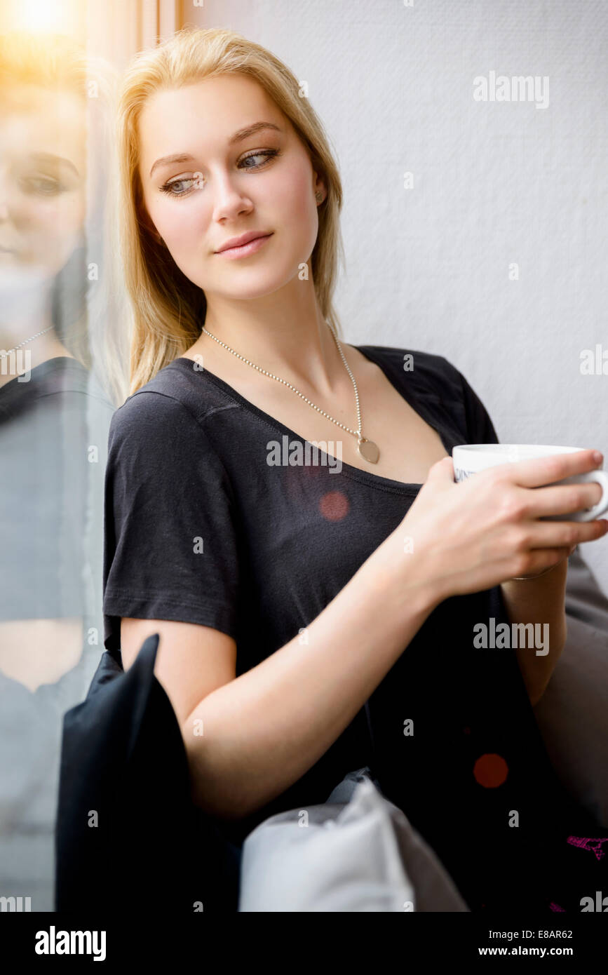Giovane donna di bere il caffè mentre guardando fuori della finestra Foto Stock