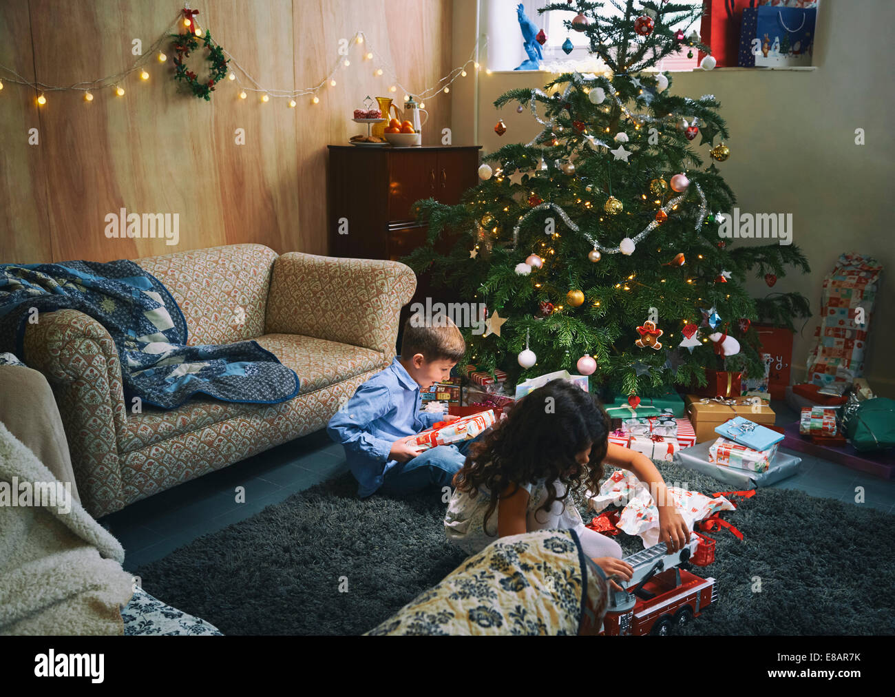 Sorella e fratello gioca con e scartare i regali di Natale sul salotto piano Foto Stock