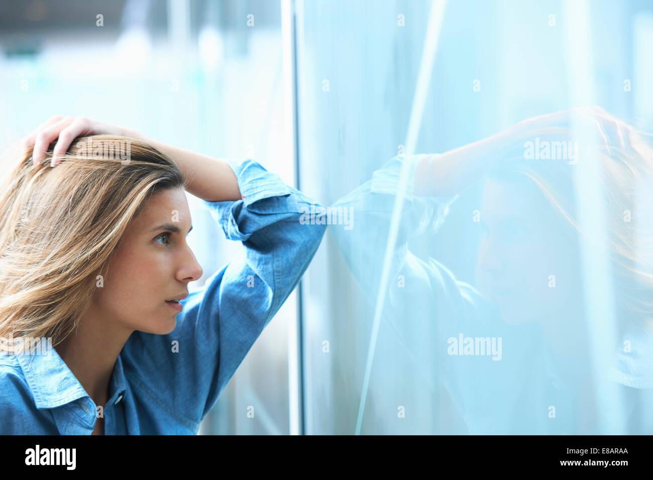 Metà adulto imprenditrice appoggiata contro la parete di vetro in ufficio con le mani nei capelli Foto Stock