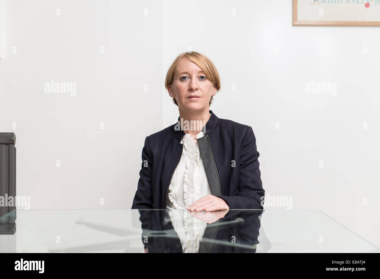 Un pelo corto business donna siede a un tavolo di vetro in una sala riunioni in un business suit cercando gravi Foto Stock