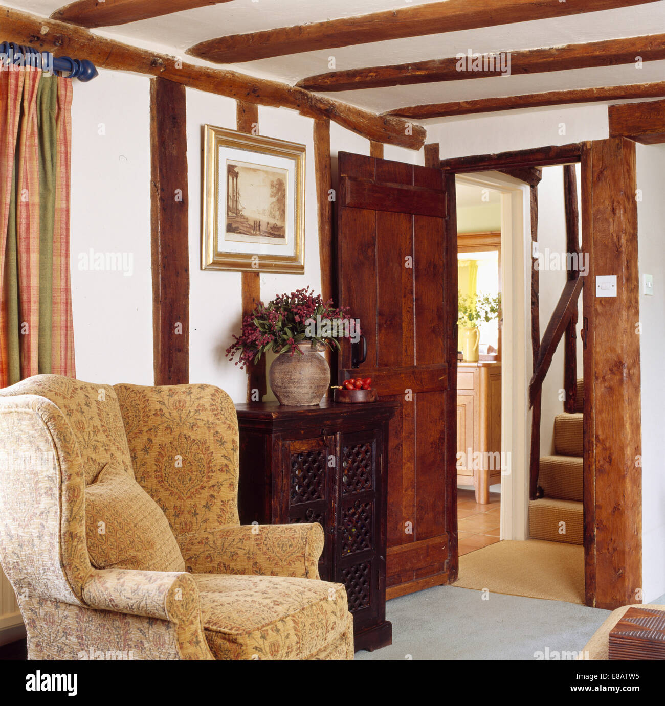 Crema ala modellato sedia in cottage di travi di soggiorno con porta aperta a hall Foto Stock