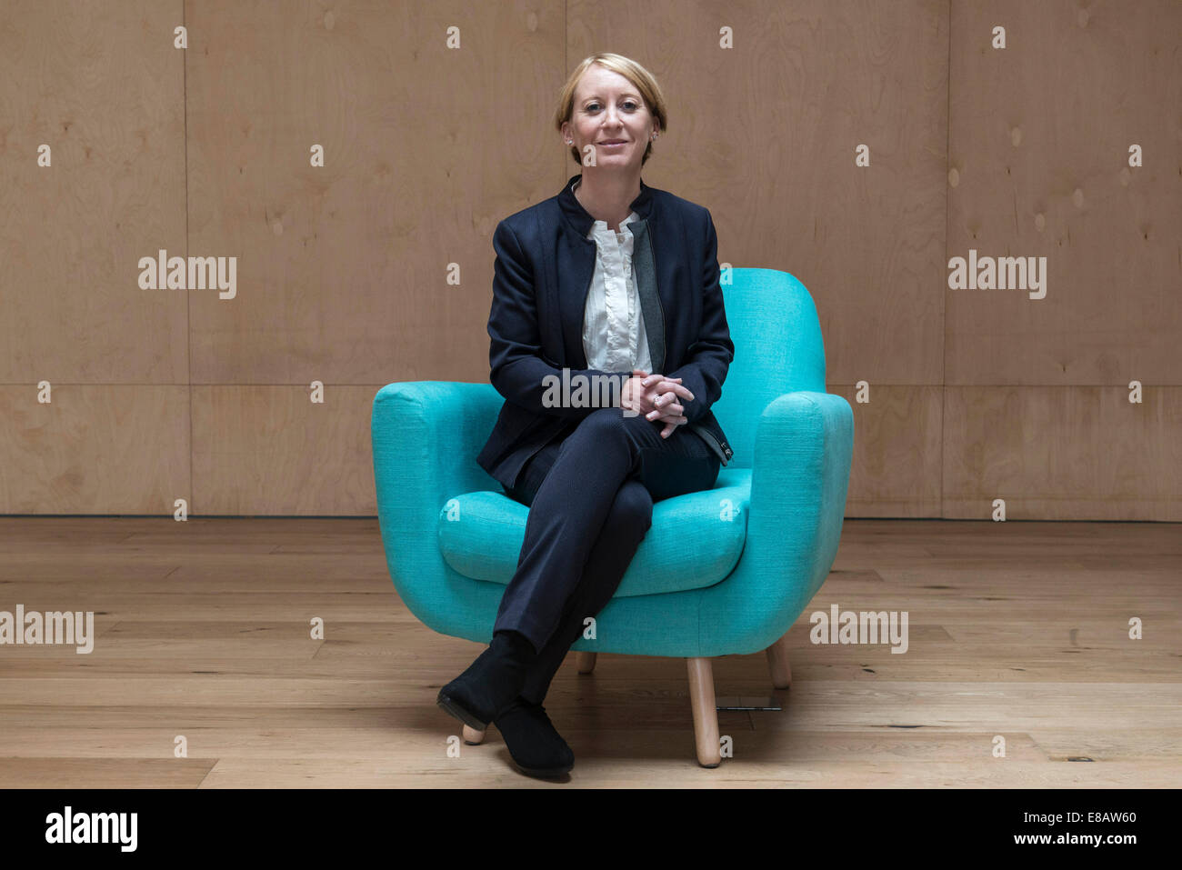 Un pelo corto business donna seduta in un funky di colore blu sedia con le gambe piegate in un business suit in una sala riunioni Foto Stock