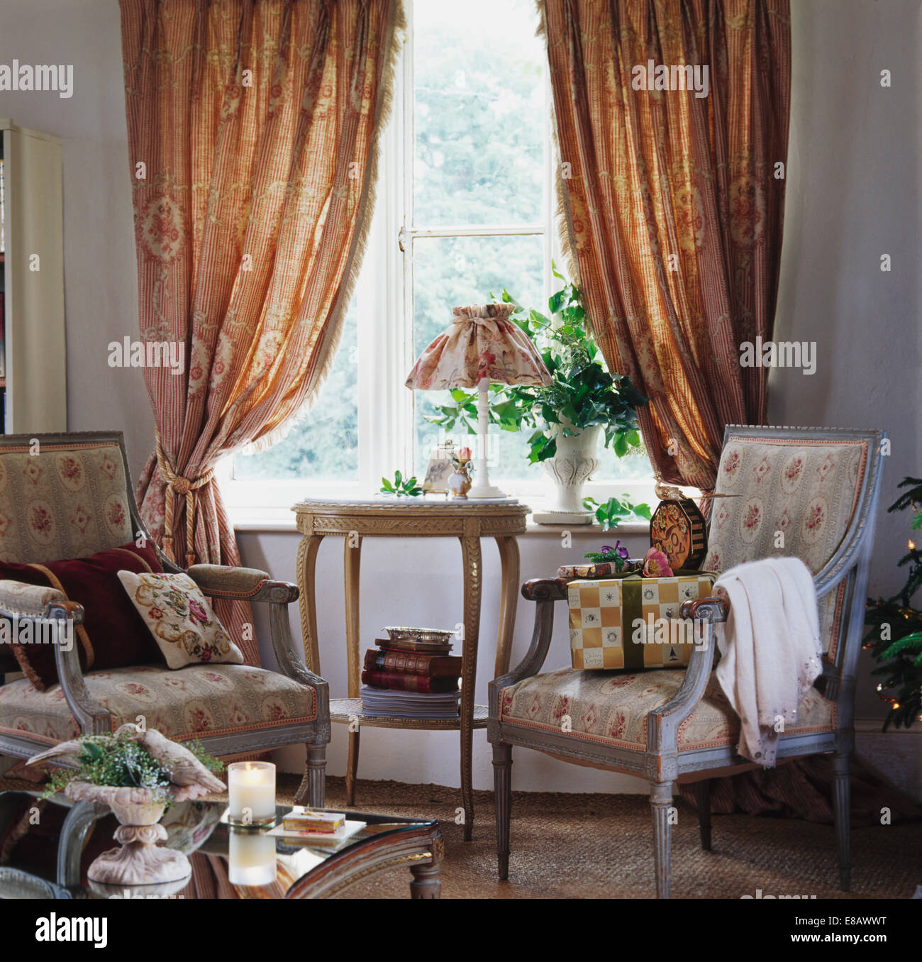 Poltrone floreali nella parte anteriore della finestra con pesanti modellato tende beige in country living room Foto Stock