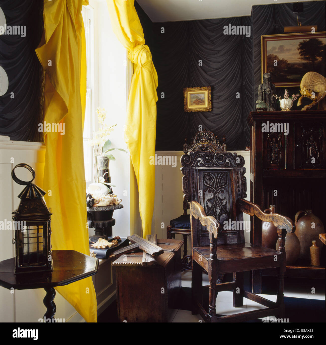 Antiquariato in legno intagliato poltrona davanti alla finestra con il giallo tende di seta nel paese hall Foto Stock