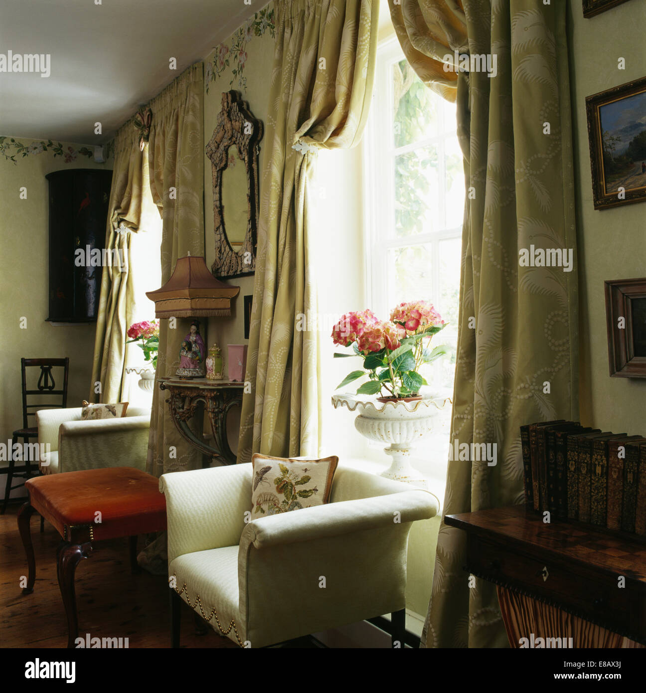 La crema poltrona davanti alla finestra con pesanti tende di seta in country living room Foto Stock