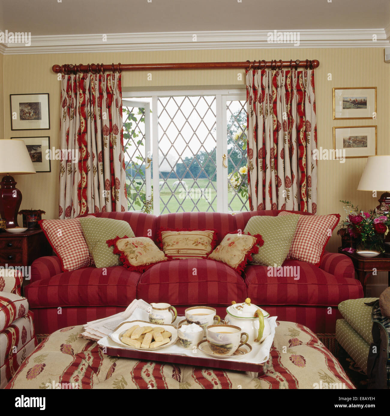 Vassoio tè su uno sgabello di fronte divano rosso e finestra di reticolo con tende a motivi geometrici in cottage soggiorno Foto Stock