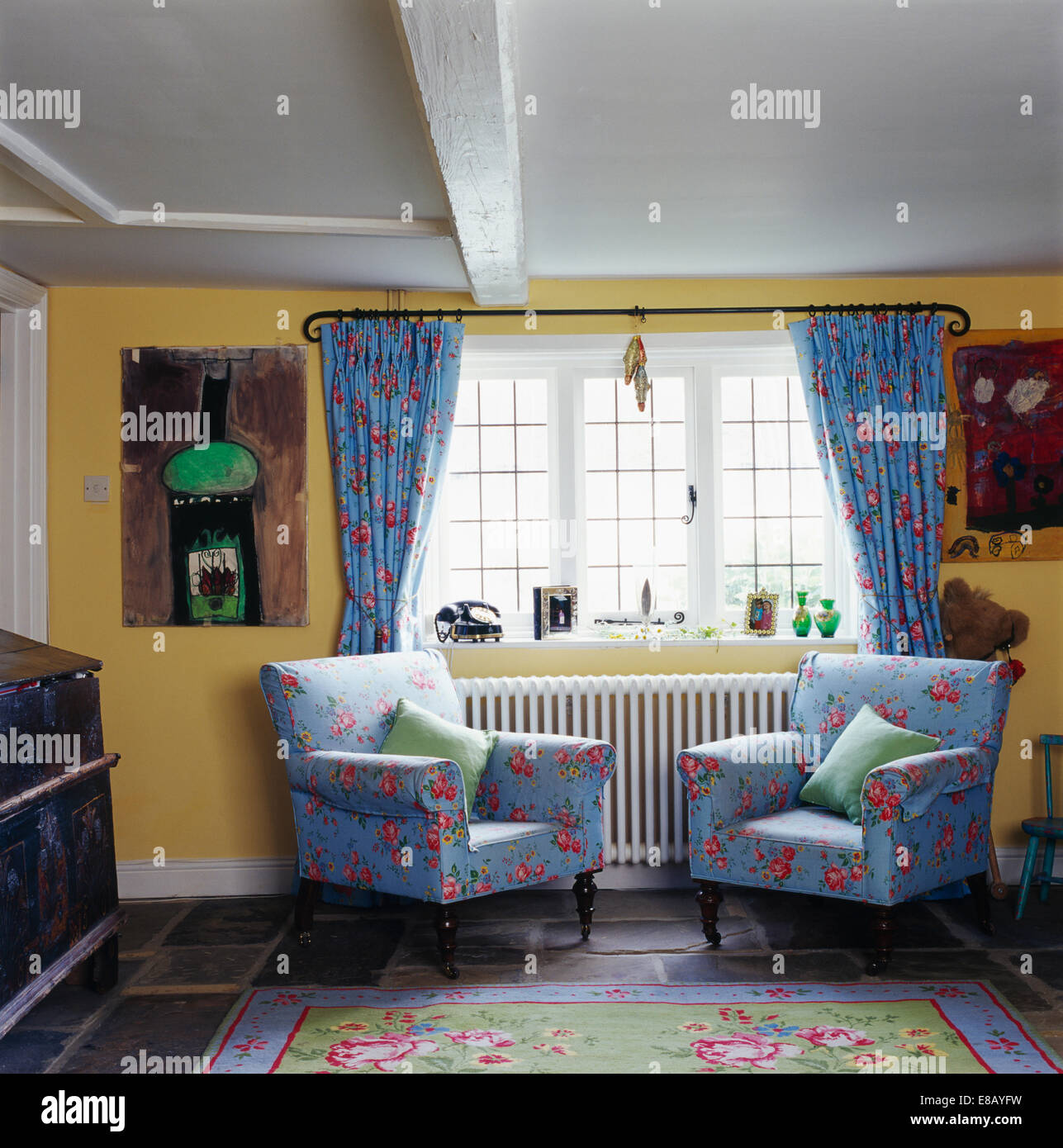 Con motivi floreali blu poltrone accanto alla finestra con abbinamento di blu tende floreali in giallo country living room Foto Stock