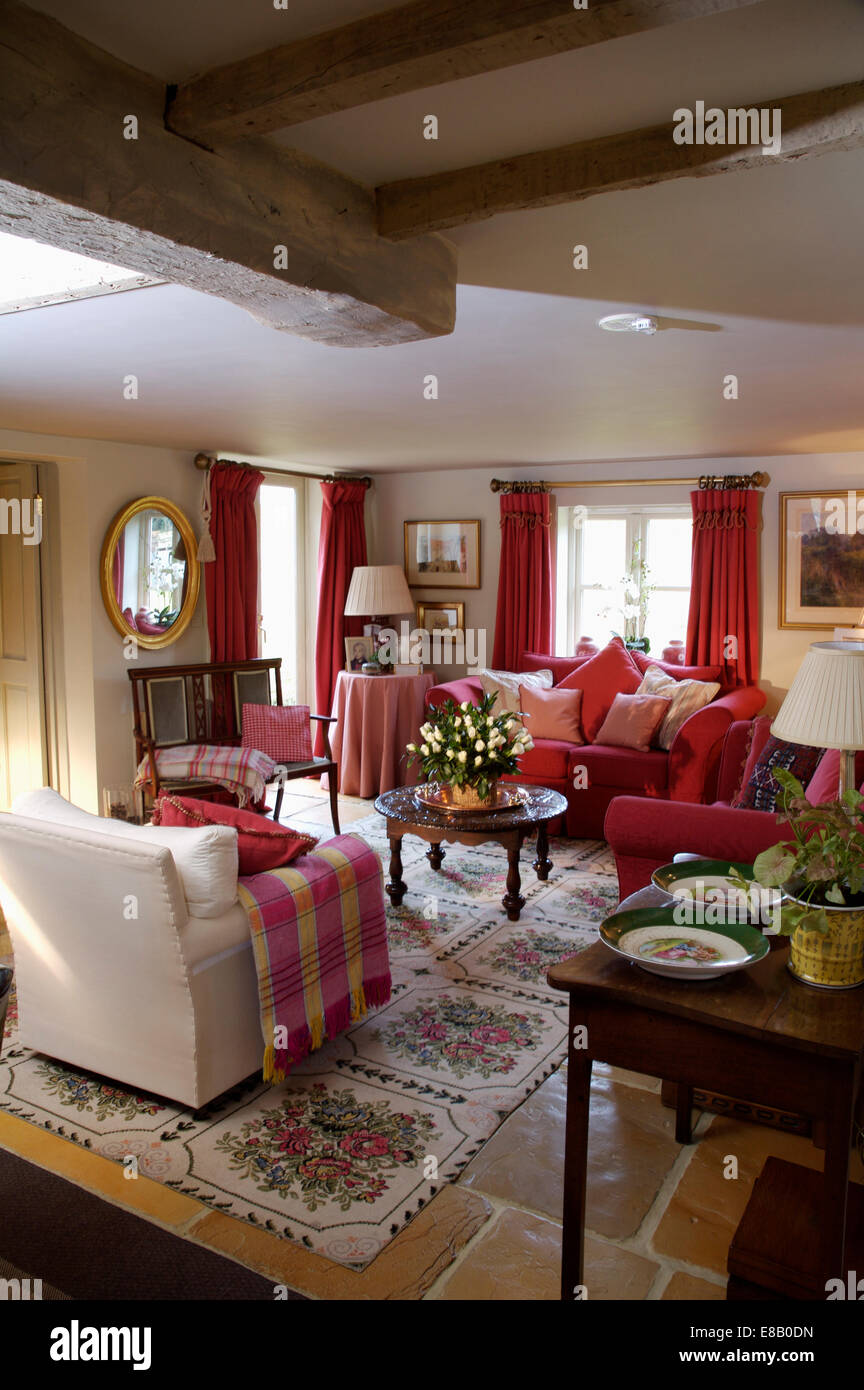 Controllare rosso buttare sulla poltrona di crema in cottage accogliente salotto con tappeti floreali sul pavimento piastrellato in pietra Foto Stock