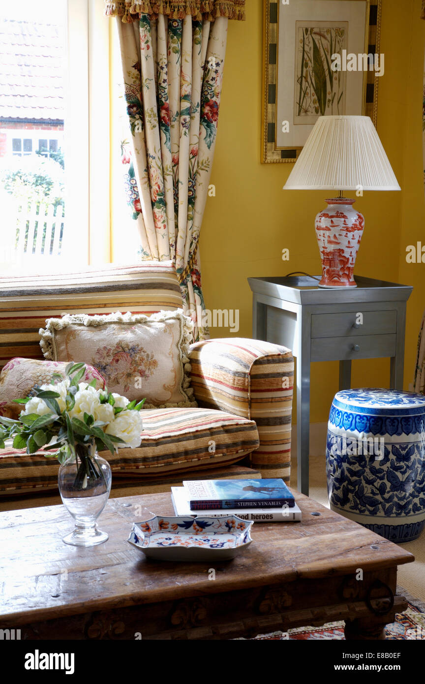 Divano a strisce e rustico tavolo da caffè in legno in giallo country living room con un alto blu+bianco vaso cinese Foto Stock