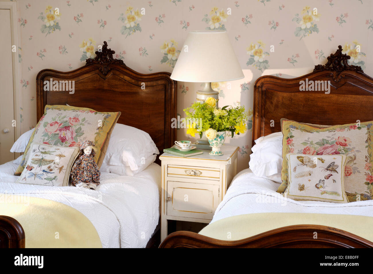 Arazzo cuscini e biancheria da letto bianca su mogano antichi letti singoli nella camera da letto del paese con carta da parati floreale Foto Stock