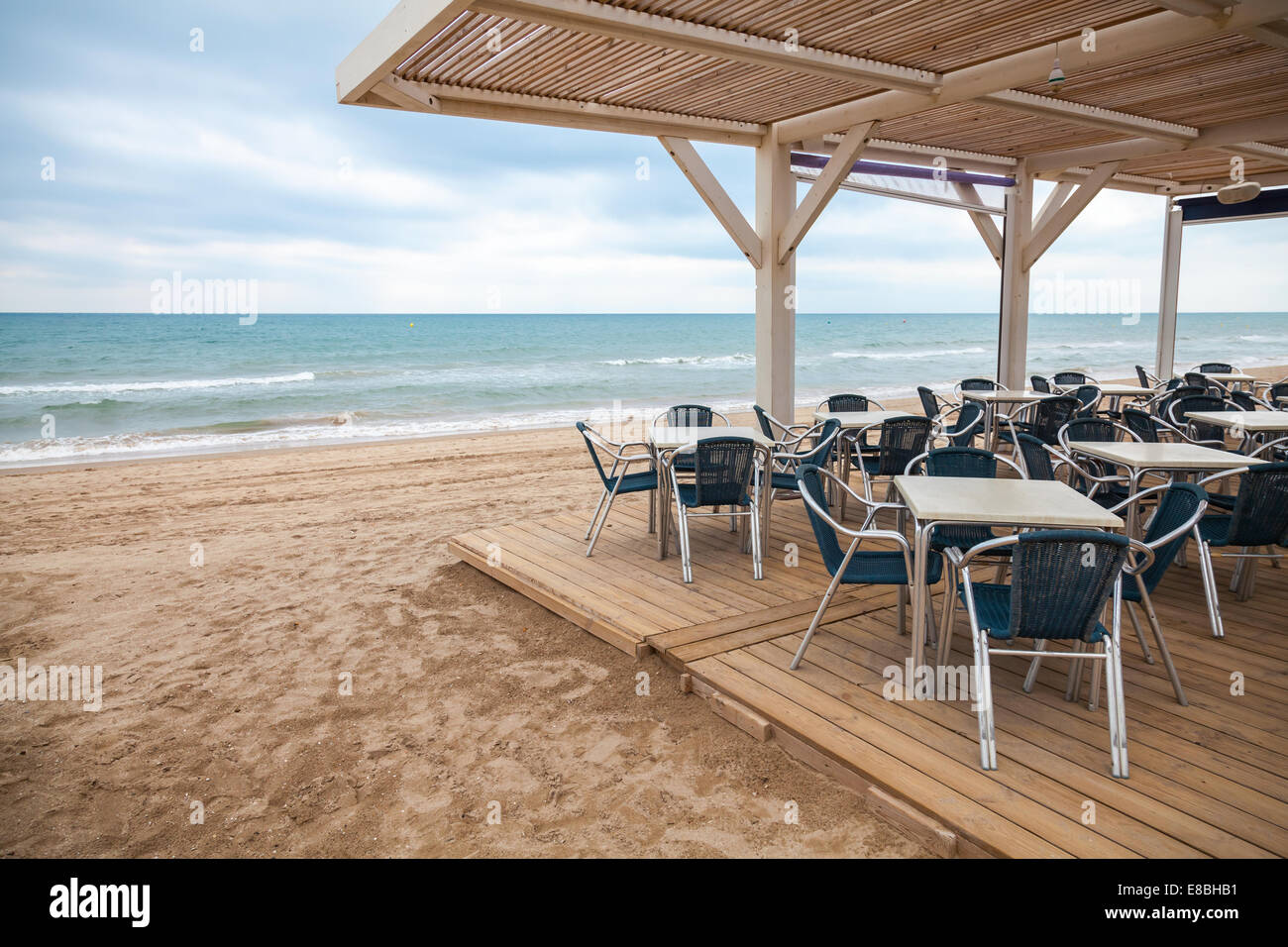 Lato mare bar interno con pavimento in legno e poltrone in metallo sulla spiaggia sabbiosa in Spagna Foto Stock