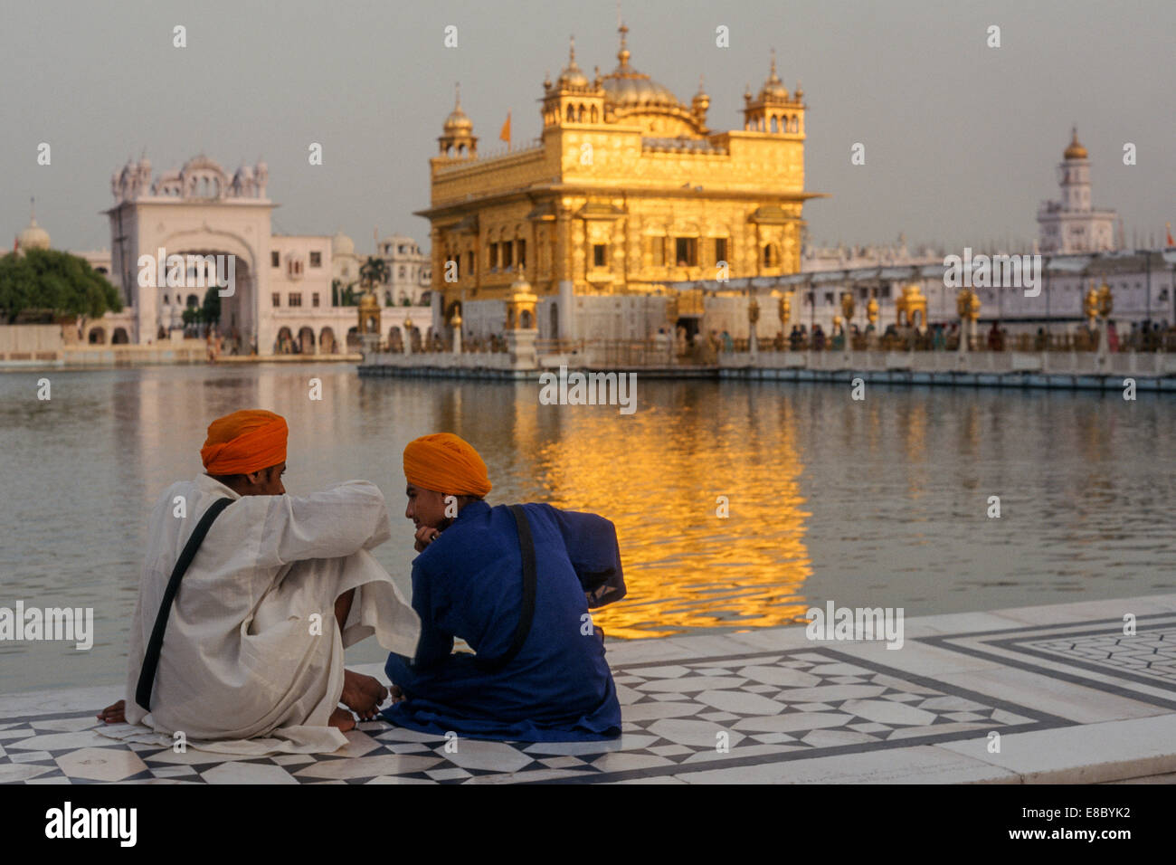 Due giovani uomini seduti di fronte al Harmandir Sahib, o Tempio d'oro, uno dei più acclamati giochi di siti per i sikh, Amritsar Punjab, India Foto Stock