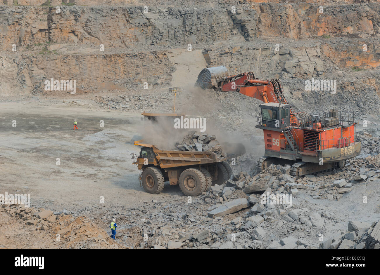 Escavatore Hitatchi carica minerale sul Caterpillar carrelli minerari in un grande cast aperto africano miniera di rame mentre il supervisore orologi Foto Stock