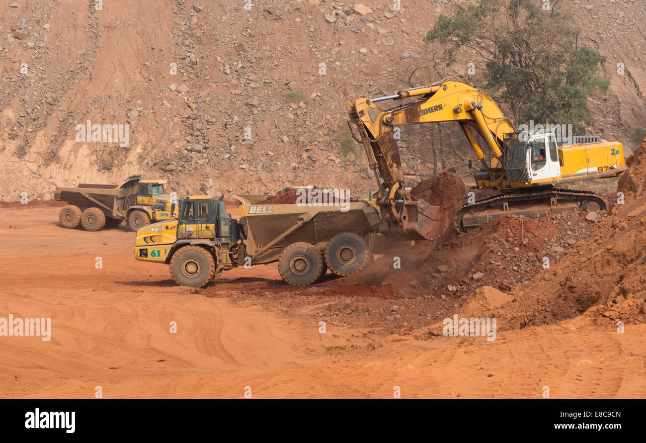 Un piccolo escavatore Liebherr carichi una campana haul carrello durante la costruzione di un deposito di acqua di stagno in corrispondenza di una superficie africana miniera di rame. Foto Stock