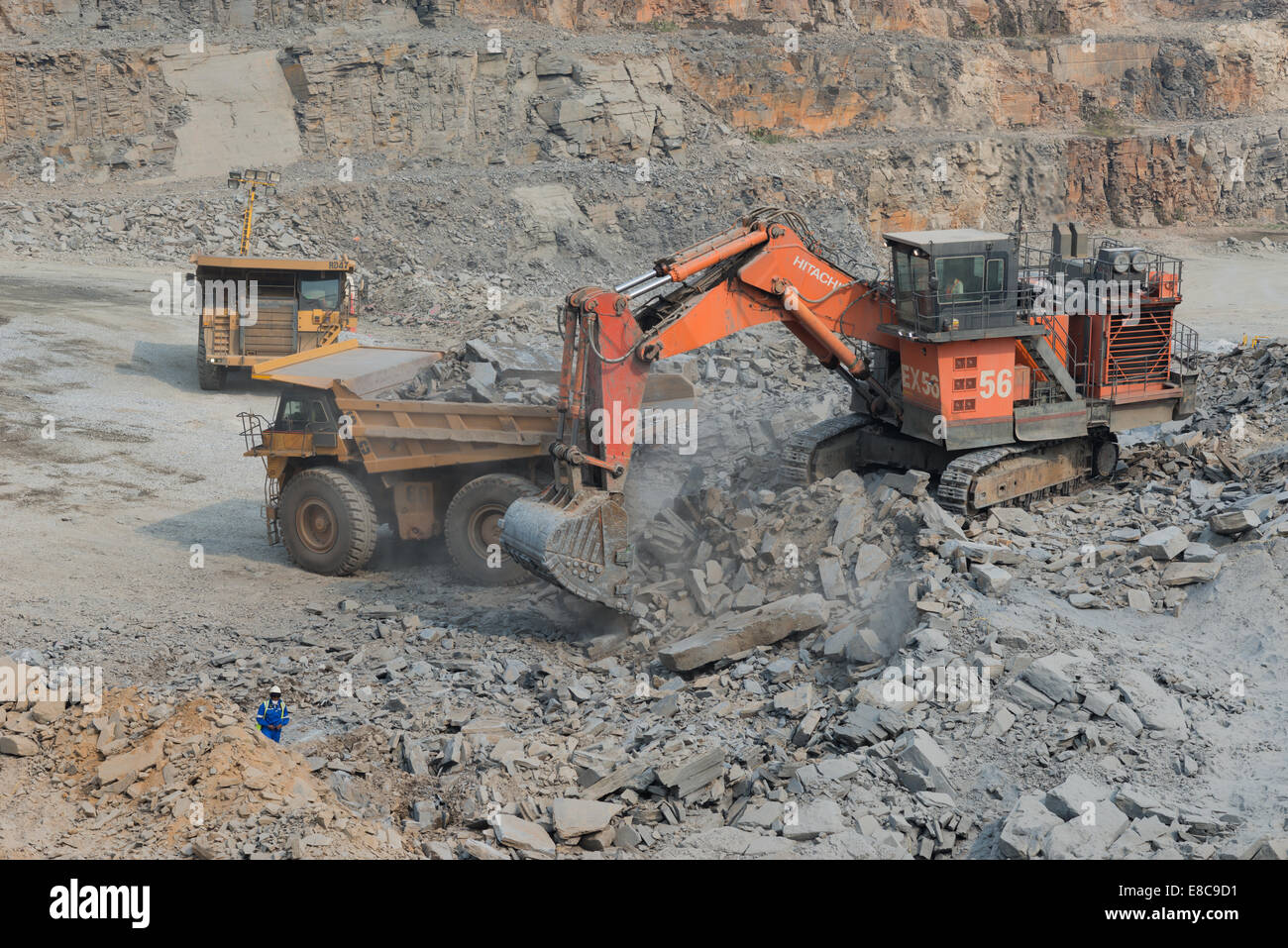 Escavatore Hitatchi carica minerale sul Caterpillar carrelli minerari in un grande cast aperto africano miniera di rame mentre il supervisore orologi Foto Stock