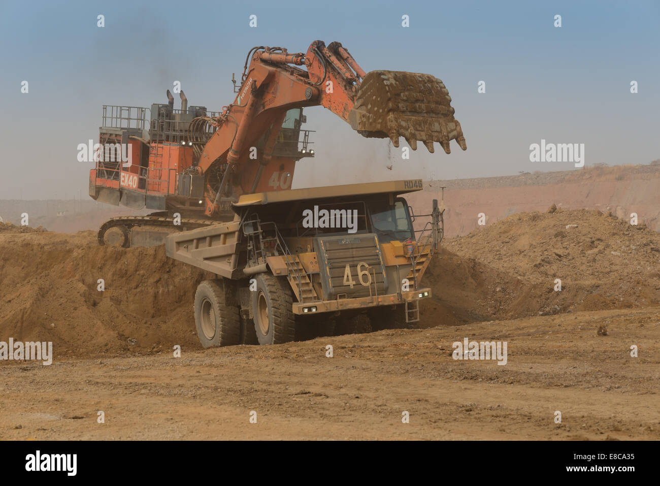 Un arancione Hitatchi escavatore rifiuti carichi di roccia e il suolo in un Caterpillar carrello minerario in un grande cast aperto africano miniera di rame. Foto Stock