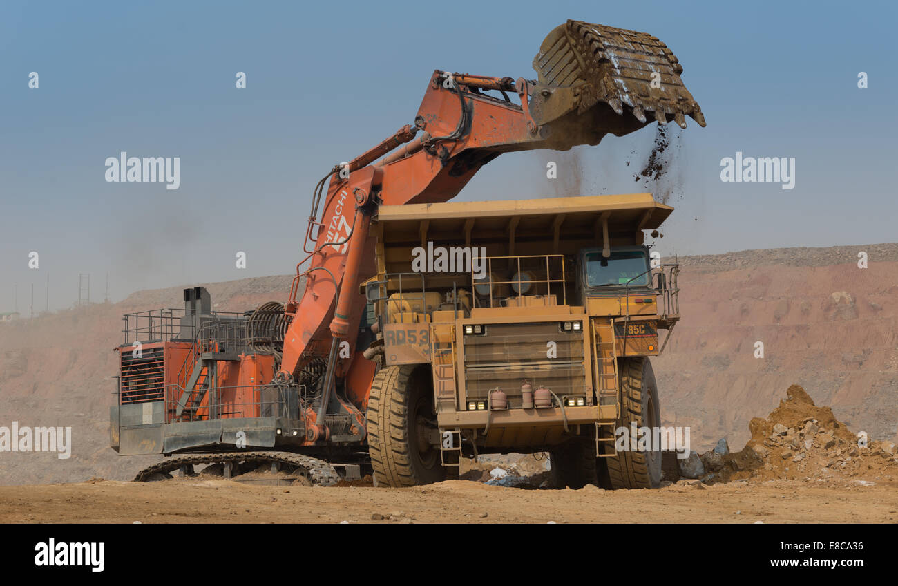 Un arancione Hitatchi escavatore rifiuti carichi di roccia e il suolo in un Caterpillar carrello minerario in un grande cast aperto africano miniera di rame. Foto Stock