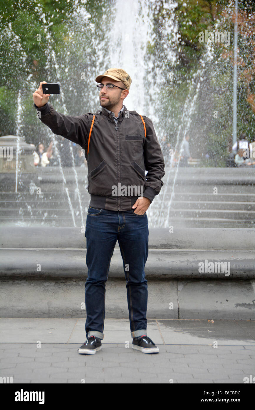 Un turista maschio in un cappello di prendere una selfie vicino alla fontana di Washington Square Park nel Greenwich Village di New York City Foto Stock