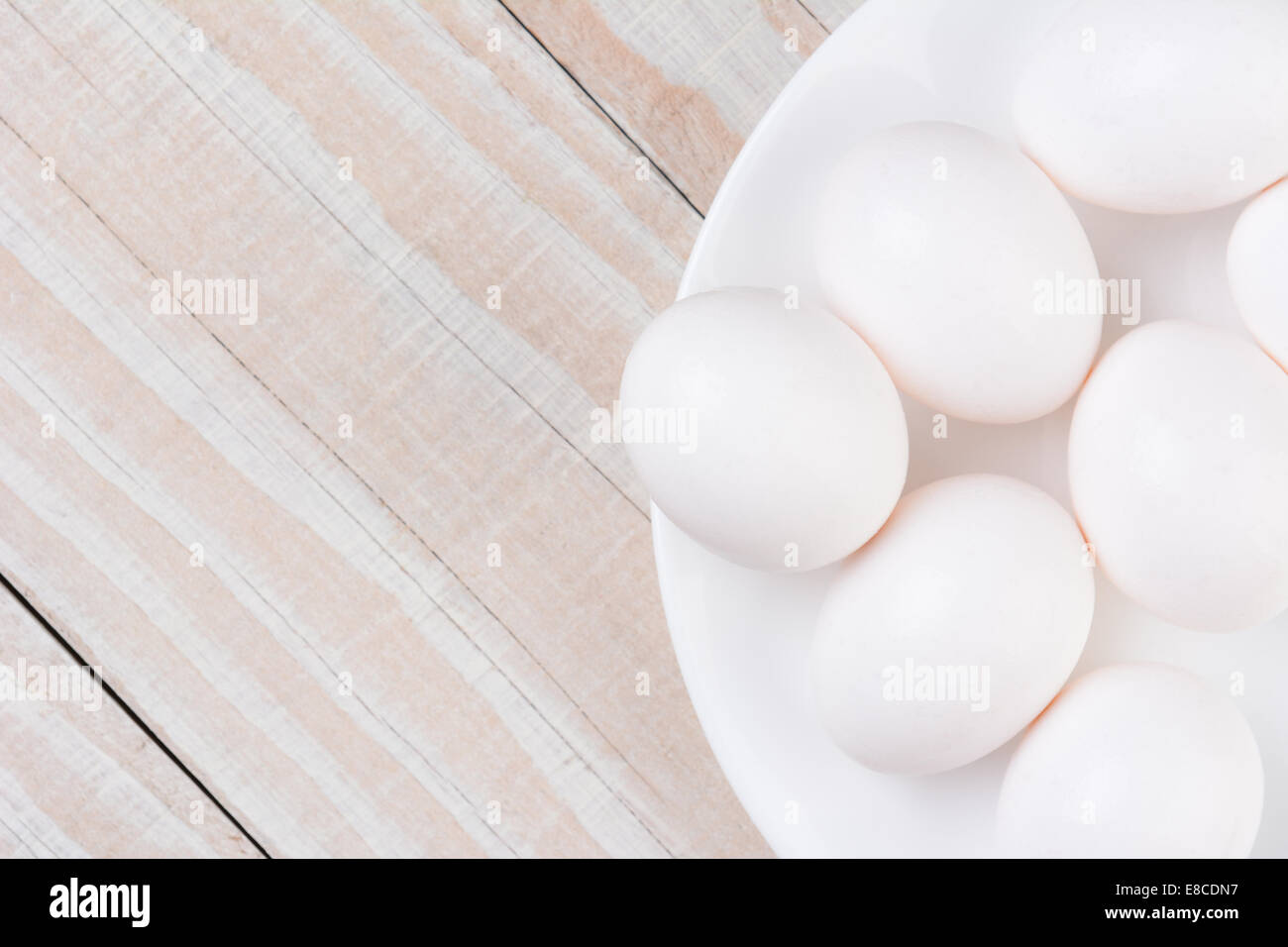 Elevato angolo di visione di un bianco ciotola riempita con le uova bianche su un bianco rustico in legno tavolo da cucina. Formato orizzontale con spazio di copia Foto Stock