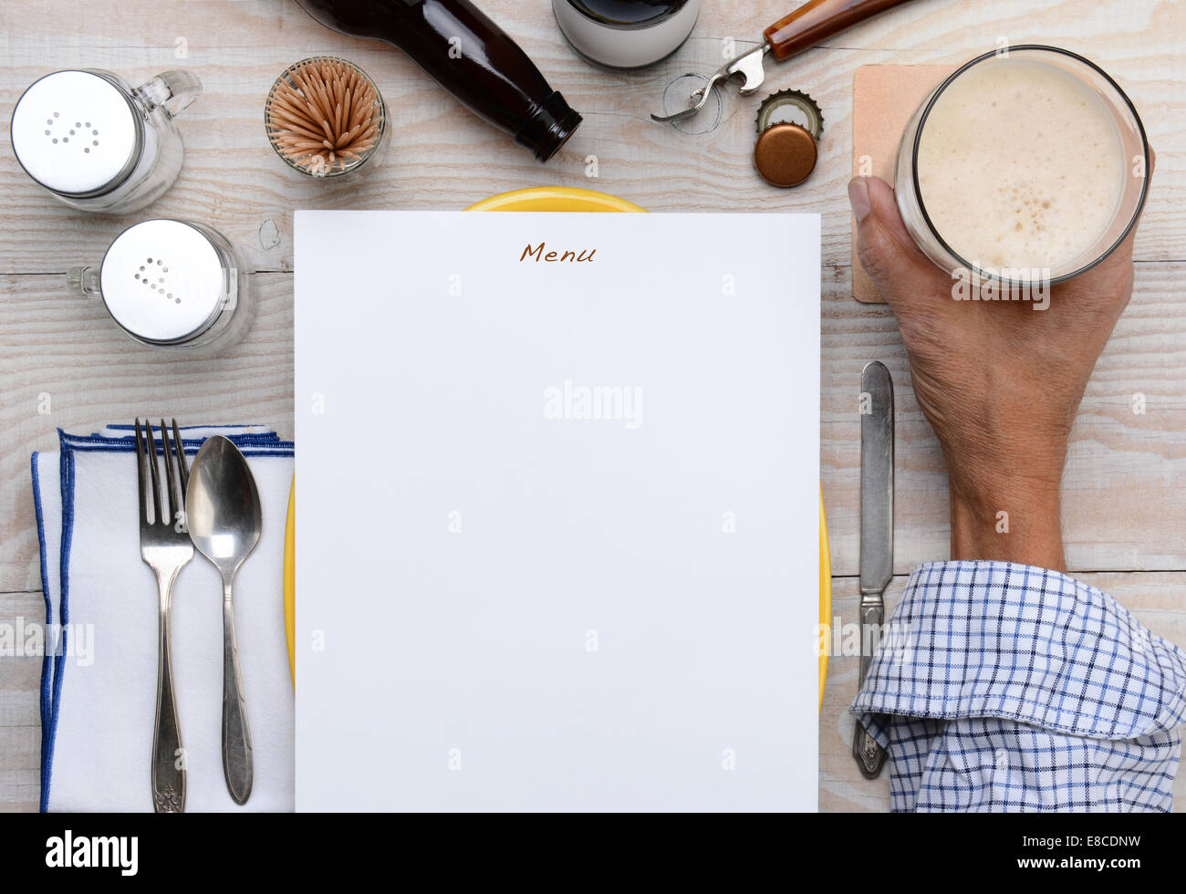Alta angolazione di un uomo con il suo bicchiere di birra su di una tavola di un ristorante con un menu vuoto davanti a lui. Solo la mano dell'uomo Foto Stock