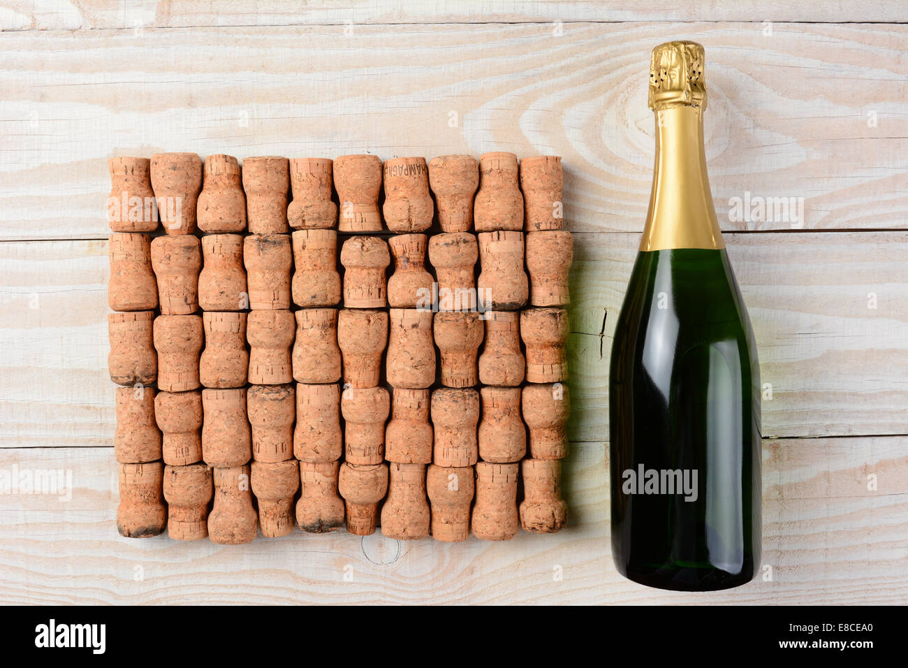 Alta angolazione di una bottiglia di champagne posa accanto ad un grande gruppo di tappi disposti in ranghi su un dipinto di bianco tavola di legno. Foto Stock