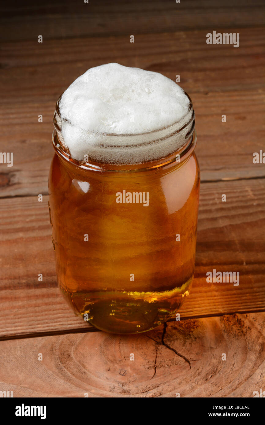 Bicchiere di birra in un paese impostazione bar servita in un barattolo di inscatolamento. Formato verticale su un legno rustico sfondo. Foto Stock