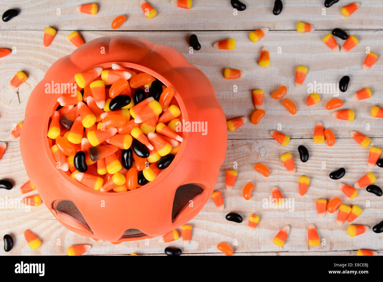 Alta angolazione di una plastica zucca di Halloween riempito con la caramella in un bianco tavola in legno rustico. Formato orizzontale con cereali caramellati Foto Stock